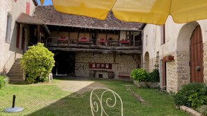 Un edificio de piedra tradicional con balcón de madera, una escalera y un área de estar cubierta al aire libre.