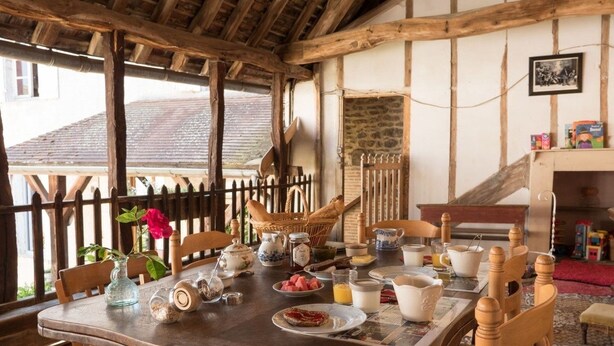 Un comedor rústico con una mesa de madera preparada para el desayuno, rodeada de sillas de madera.