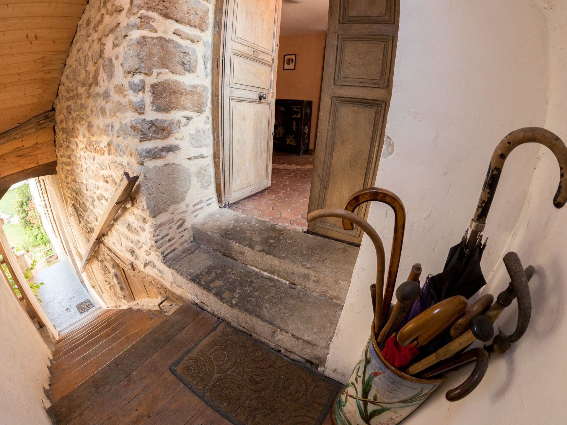 A rustic staircase leading to a room with a wooden door and a cane leaning against the wall.