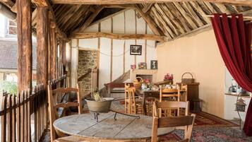 Un coin repas rustique avec une table ronde en bois, plusieurs chaises en bois, un mur en pierre et un rideau rouge.