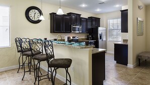 Une cuisine moderne avec des meubles de couleur sombre, un îlot central, des tabourets de bar et une horloge au mur.