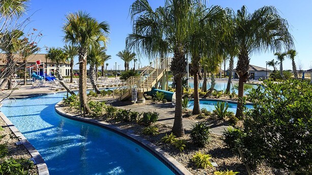 Un espace piscine agrémenté de palmiers, d’un toboggan aquatique et d’un ciel d’un bleu limpide.