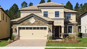 Une maison à deux étages avec une façade en pierre, une porte de garage beige et un toit recouvert de tuiles.