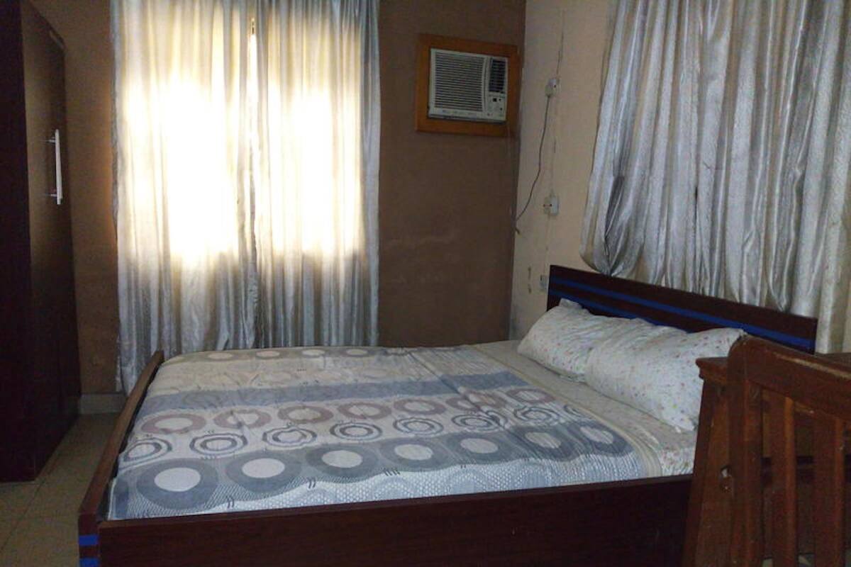 Un dormitorio con cama, cortinas, unidad de aire acondicionado y cabecera de madera.