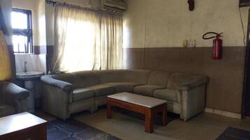Un salón con sofá, una mesita, alfombra estampada, ventana con cortinas y extintor de incendios en la pared.