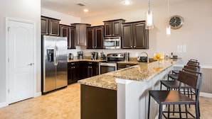 A modern kitchen with dark wooden cabinets, stainless steel appliances, and a granite countertop island with bar stools. - Je54200 - Champions Gate Resort - 8 Bed 5 Baths Villa (Davenport)