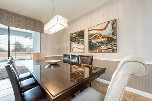 A dining room with a glass table, leather chairs, and two abstract paintings on the wall.