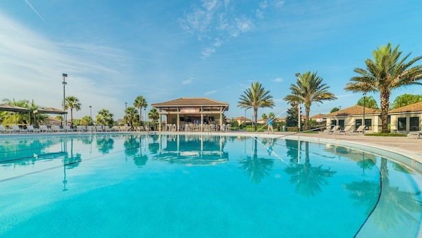A large outdoor swimming pool with lounge chairs and palm trees, surrounded by buildings with a Mediterranean architectural style. - Je54200 - Champions Gate Resort - 8 Bed 5 Baths Villa (Davenport)