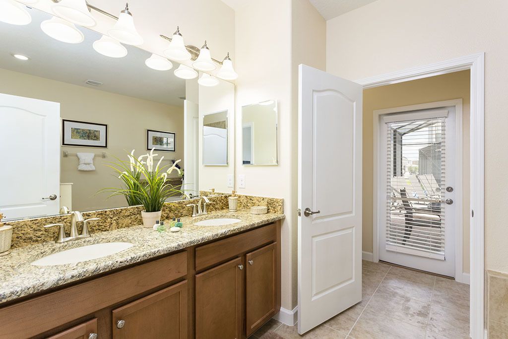 A bathroom with two sinks, a large mirror, and a potted plant. There is a door leading to a balcony with a view of the outside.