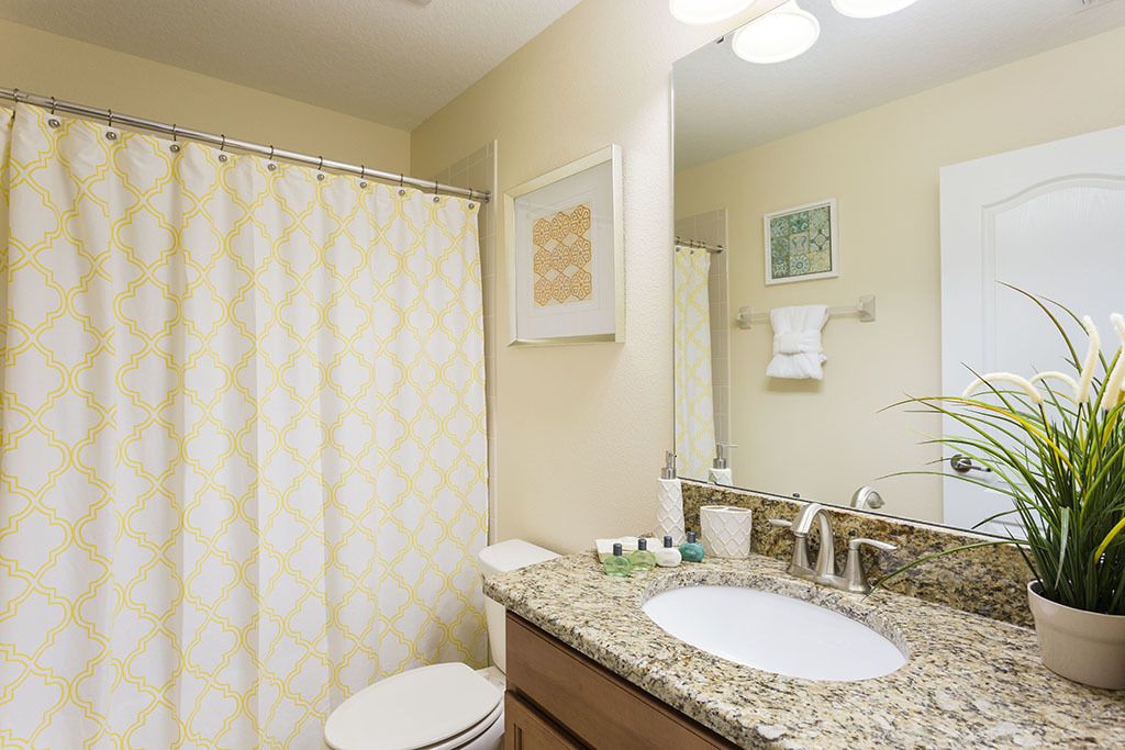 A bathroom with a patterned shower curtain, a sink with a mirror, and a potted plant.