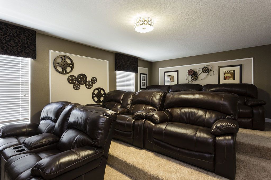 A home theater room with a large leather reclining sofa and a smaller chair, carpeted floor, and wall-mounted decorations.