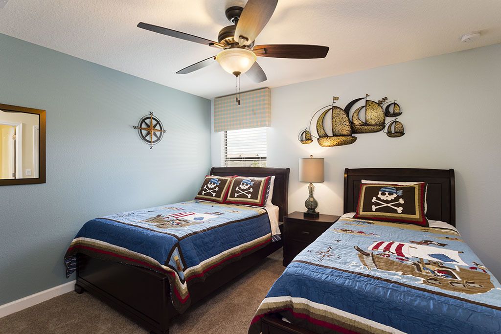 A bedroom with two beds, a ceiling fan, a compass wall decoration, and a window with blinds.