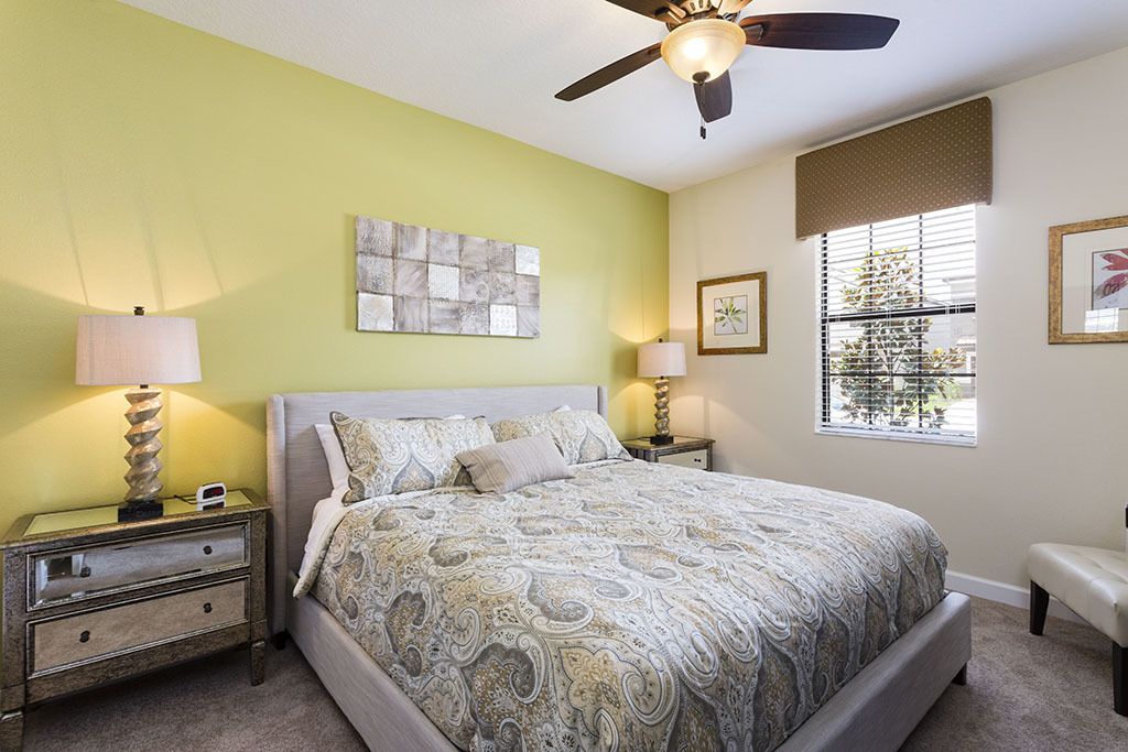 A bedroom with a bed, two nightstands, a ceiling fan, a window with blinds, and artwork on the walls.