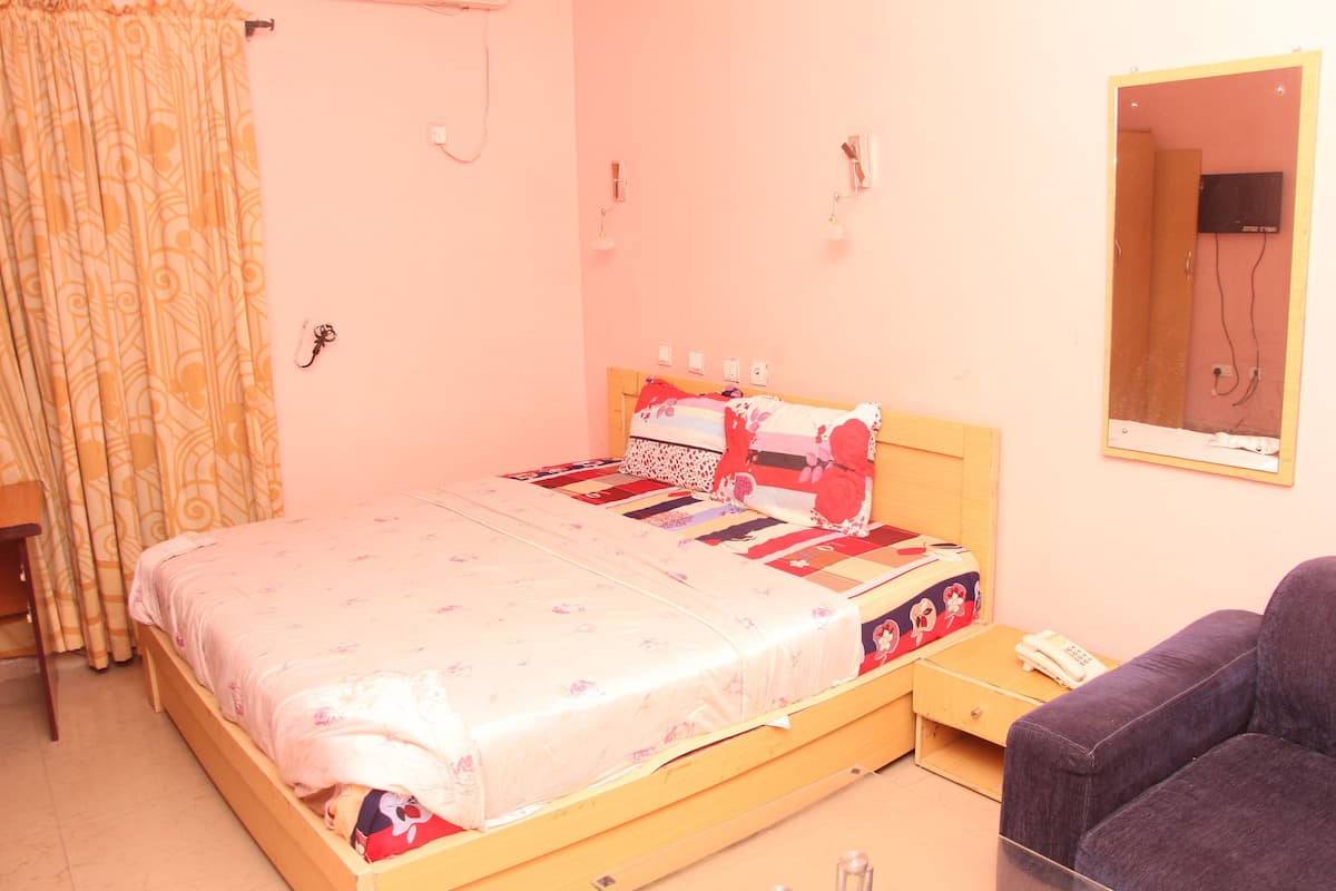 A bedroom with a wooden bed, a bedside table, a chair, a mirror, and a curtain.