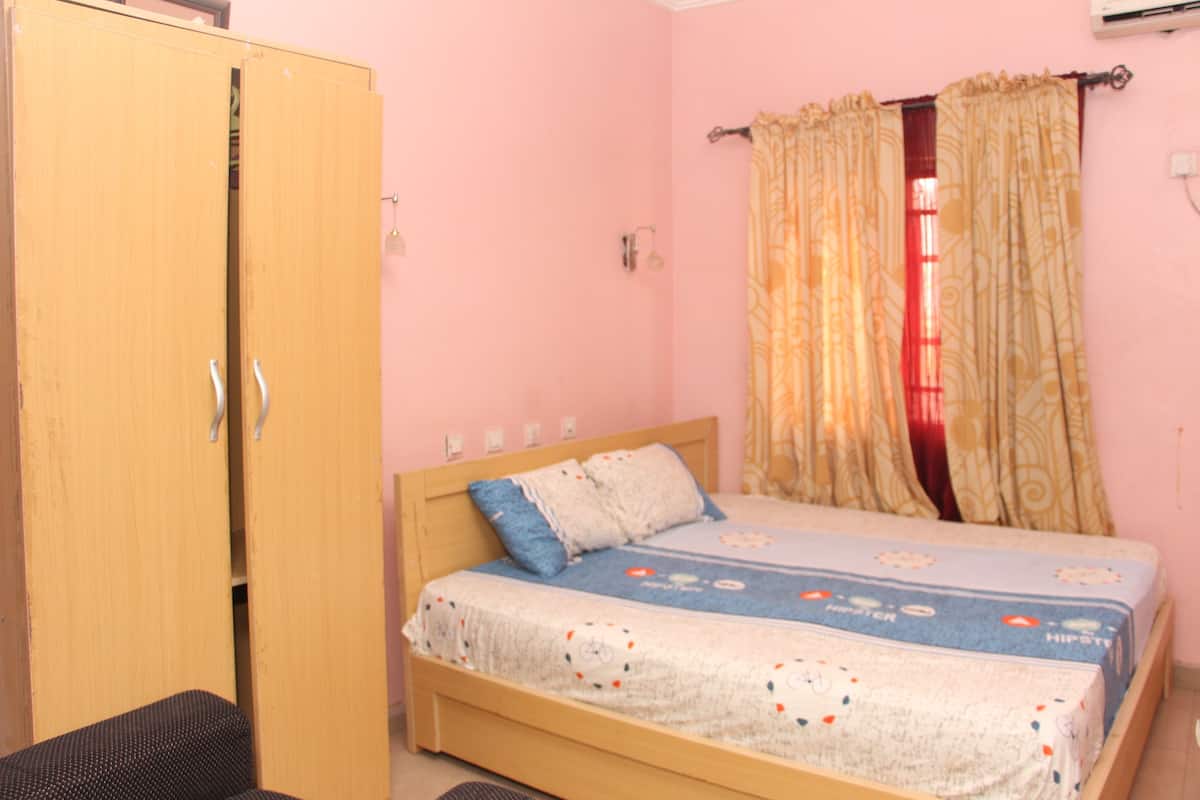 A bedroom with a wooden wardrobe, a bed with patterned bedding, and a curtain.