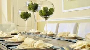 Une table à manger dressée avec de l’argenterie blanche, des serviettes pliées et trois vases en verre transparent contenant des objets verts.