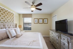 Une chambre à coucher comprenant un lit, une commode, un ventilateur de plafond et un téléviseur.
