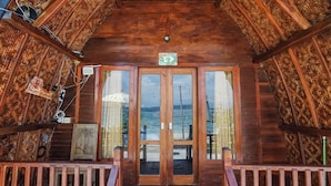 Una cabaña de madera con balcón, una puerta de madera con un letrero de número y vista al mar.