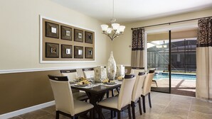 A dining area with a large table set for six, surrounded by chairs. There is a chandelier above the table and a large vase on it. The room has a large sliding glass door leading to a pool area. - Je58579 - Champions Gate Resort - 8 Bed 5 Baths Villa (Davenport)