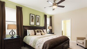 Un dormitorio con cama, mesitas de noche, una silla y un ventilador de techo.