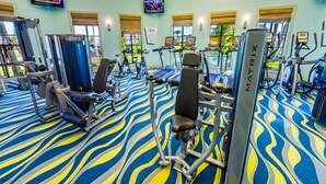 Ett gym med olika typer av träningsutrustning, inklusive löpband och styrketräningsmaskiner, och ett mönstrat golv.