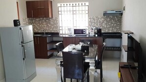 A compact kitchen with a refrigerator, microwave, and coffee maker. There is a dining table with chairs and a small island with a sink. - Northern Pearl Luxury Apartments (Mont Choisy)