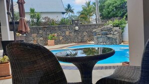 A view of a stone wall and a swimming pool from a room with wicker furniture. - Northern Pearl Luxury Apartments (Mont Choisy)