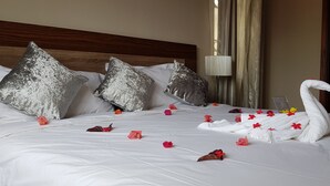 A neatly made bed with pillows, a swan-shaped towel, and scattered flowers. - Northern Pearl Luxury Apartments (Mont Choisy)