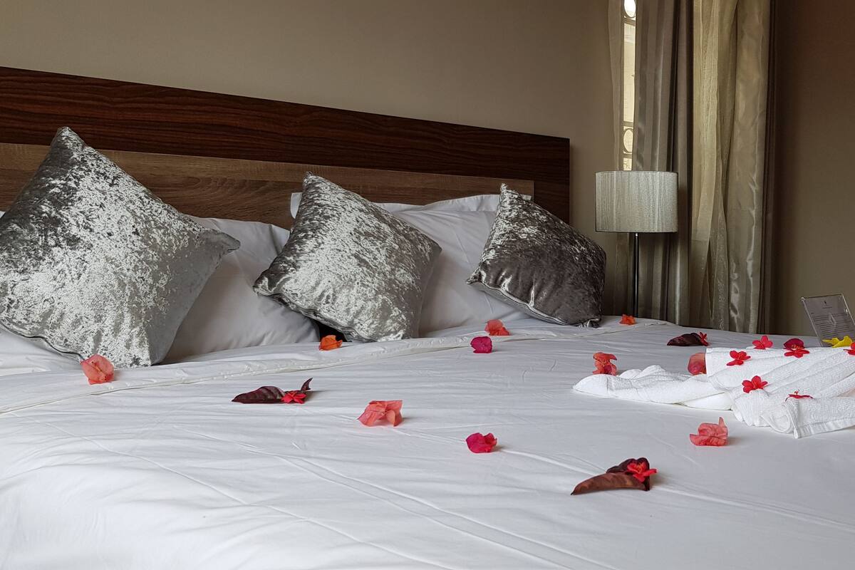 Ein ordentlich bezogenes Bett mit Kissen, ein schwanenförmiges Handtuch und verstreute Blumen.