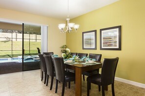 A dining area with a wooden table, black chairs, a chandelier, and two framed artworks on the wall.