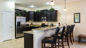 Una cocina moderna con armarios oscuros, electrodomésticos de acero inoxidable, encimera de granito y una zona de bar con sillas de cuero.