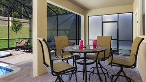 Un patio al aire libre con una mesa redonda y cuatro sillas, un jacuzzi y vista a un área verde.