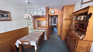 A cozy room with a dining table, chairs, a wooden bench, a stone wall, a clock, and wooden cabinets.