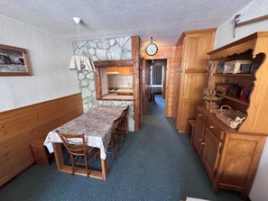 A cozy room with a dining table, chairs, a wooden bench, a stone wall, a clock, and wooden cabinets.