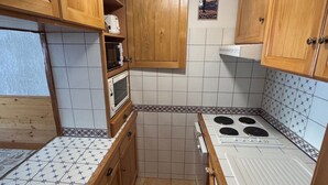 A compact kitchen with wooden cabinets, a microwave, a stove, and patterned tiles.