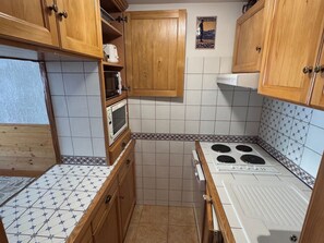 A compact kitchen with wooden cabinets, a microwave, a stove, and patterned tiles.