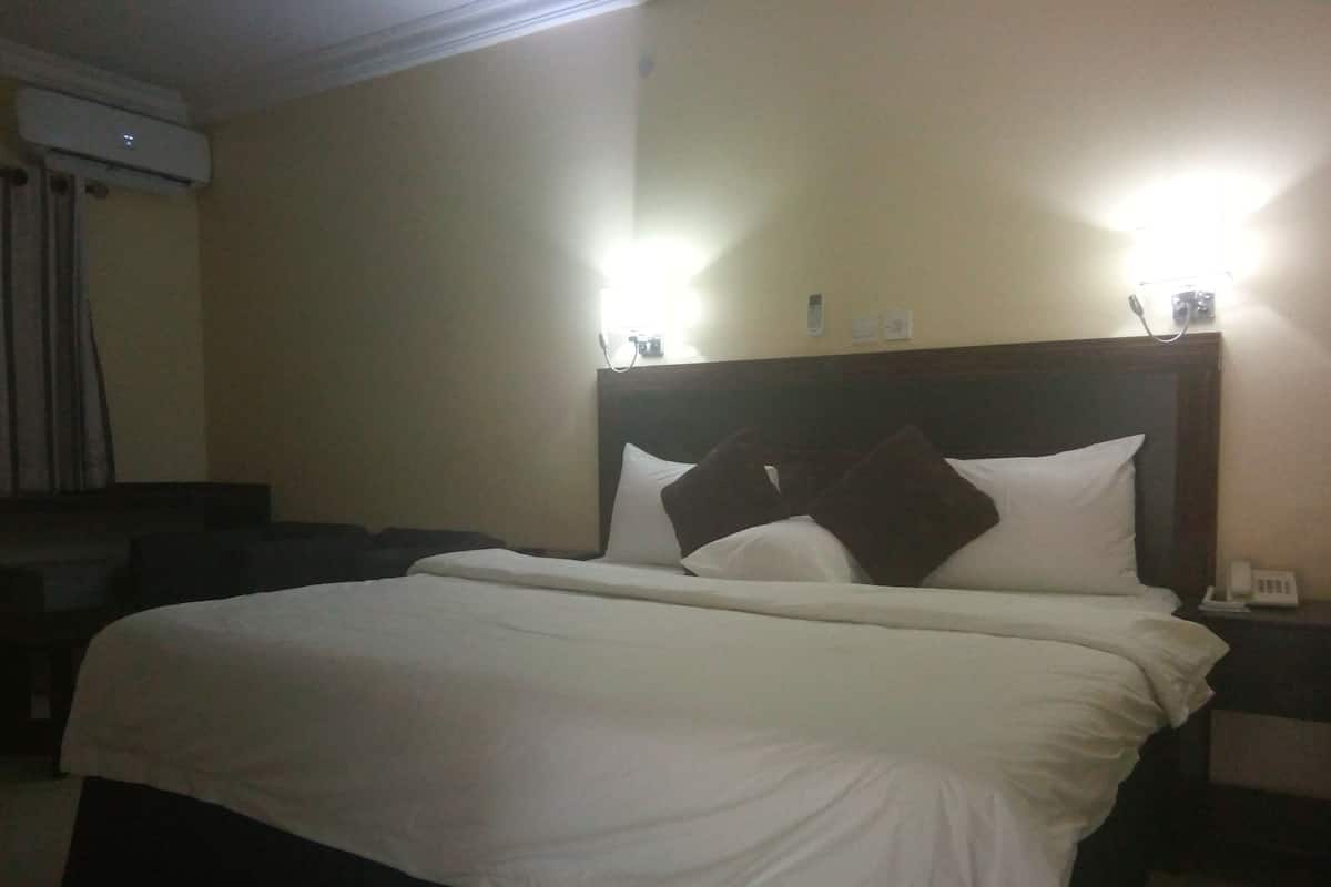 Hotellihuone, jossa on suuri sänky, yöpöytä lampun kanssa ja ilmastointilaite seinällä.