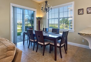A dining area with a table and chairs, a chandelier, and a view through large windows.