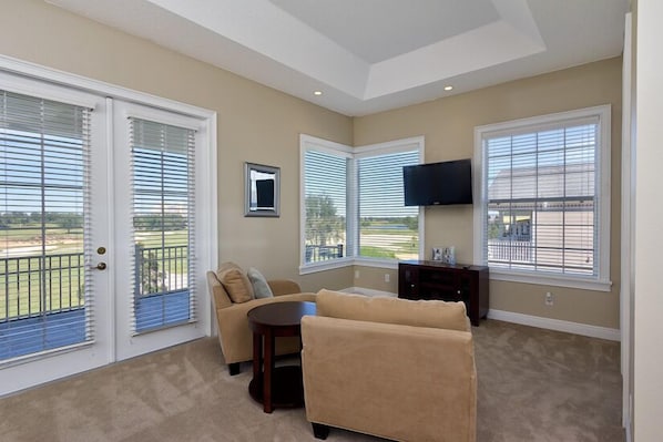 A living room with beige walls, a beige sofa, a small round table, and a TV mounted on the wall.