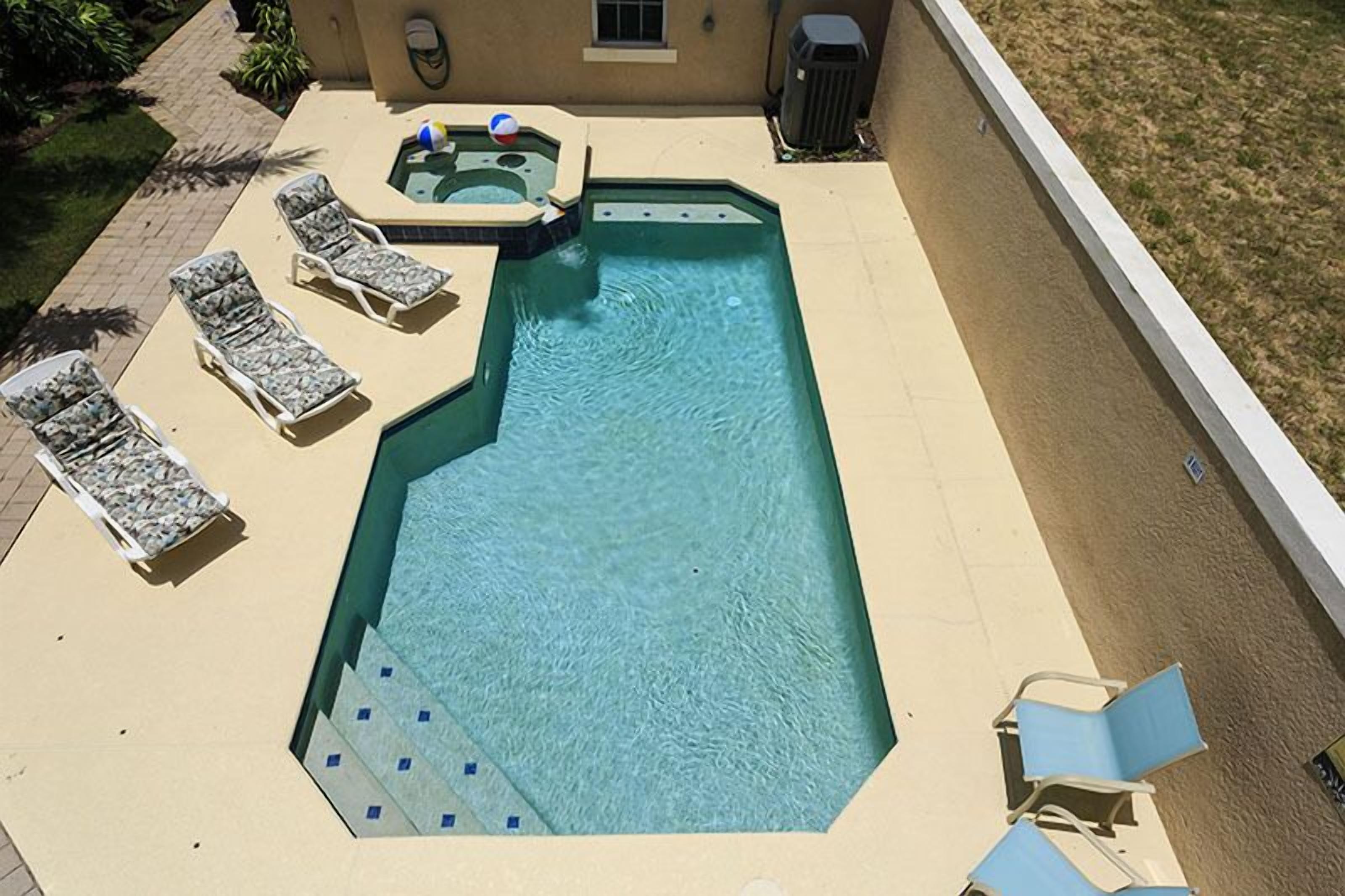 A rectangular swimming pool with a hot tub, surrounded by lounge chairs and a small deck area.