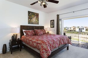 A bedroom with a large bed, a ceiling fan, a nightstand with a lamp, a painting on the wall, and a view of the outside through a sliding door. - Je52200 - Reunion Resort - 5 Bed 4 Baths Villa (Kissimmee)