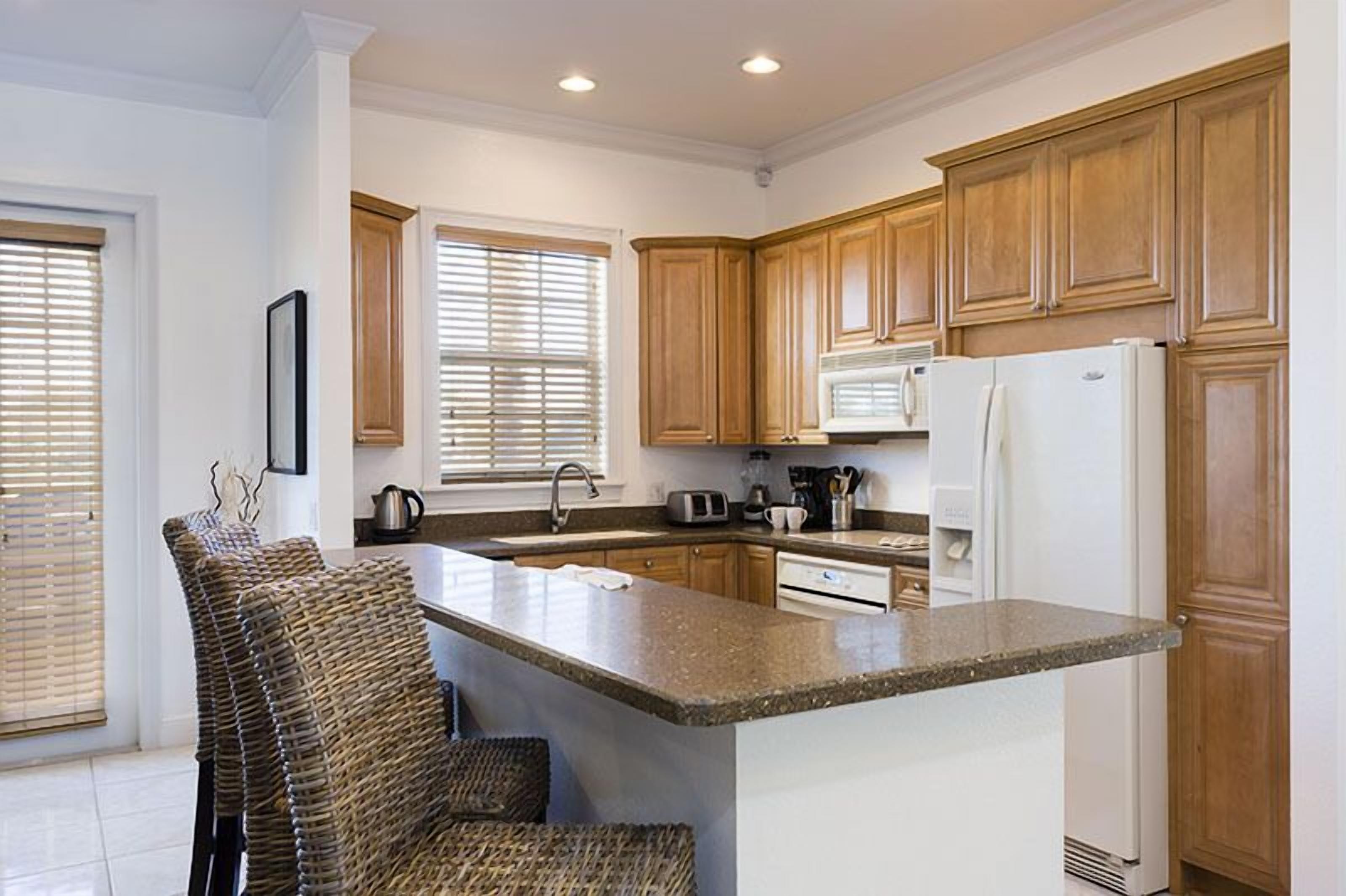 A kitchen with wooden cabinets, a granite countertop, a built-in microwave, and a refrigerator.