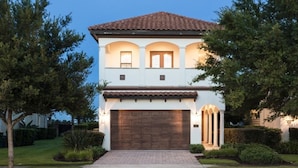 A two-story house with a brown tiled roof, a large garage door, and a well-maintained front yard with trees and shrubs.