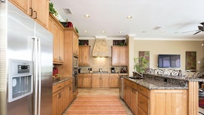 A kitchen with wooden cabinets, a stainless steel refrigerator, a granite countertop, and a stone backsplash.