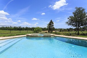 A rectangular swimming pool with a central island, surrounded by a fence and trees.