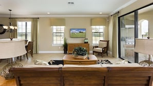 A spacious living room with a large sofa, a dining table, and a kitchen visible through a sliding glass door. - Je52915 - Reunion Resort - 5 Bed 5 Baths Villa (Kissimmee)