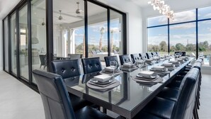 A modern dining room with a long table set for a meal, large windows, and a view of the outdoors. - Je52232 - Reunion Resort - 11 Bed 10 Baths Villa (Kissimmee)