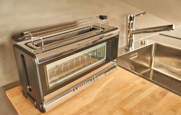 A stainless steel toaster oven with a wire rack on top, placed on a wooden cutting board. - Kitzhome City Appartements (Kitzbuhel)
