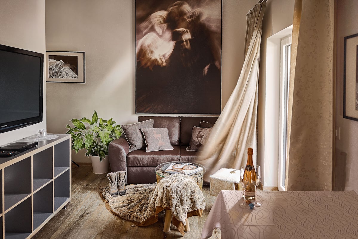 A cozy living room with a large TV, a sofa, a coffee table, and a potted plant.