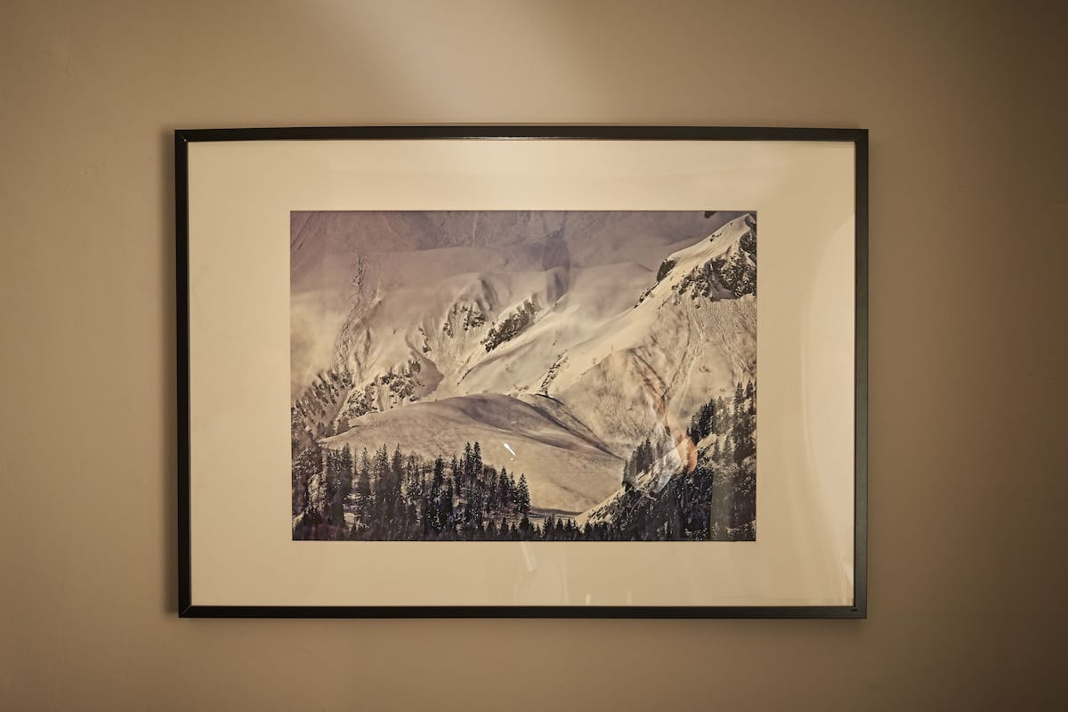 A framed photograph of a mountainous landscape with snow-covered peaks and a forested area at the base.
